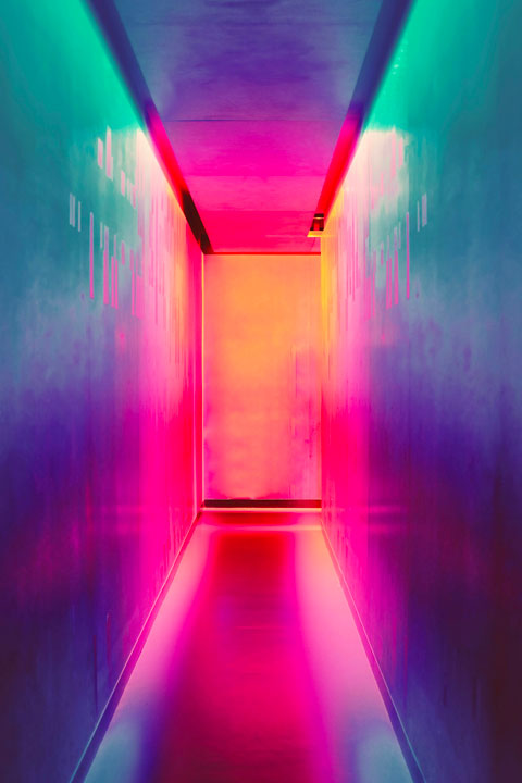 Narrow corridor glowing with pink, red and teal neon light