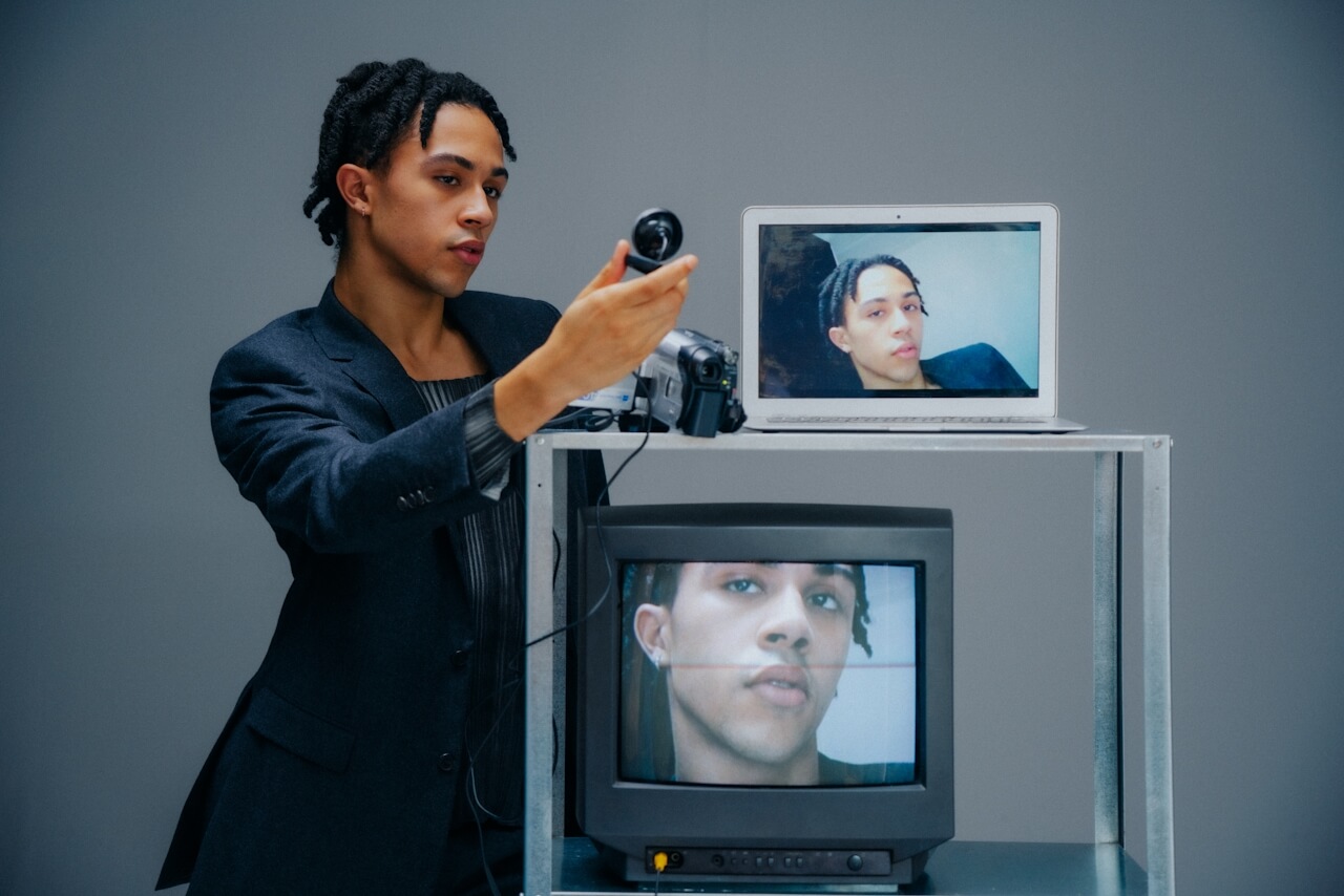 Young man filming himself with a camcorder, his face shown on a laptop and a CRT TV