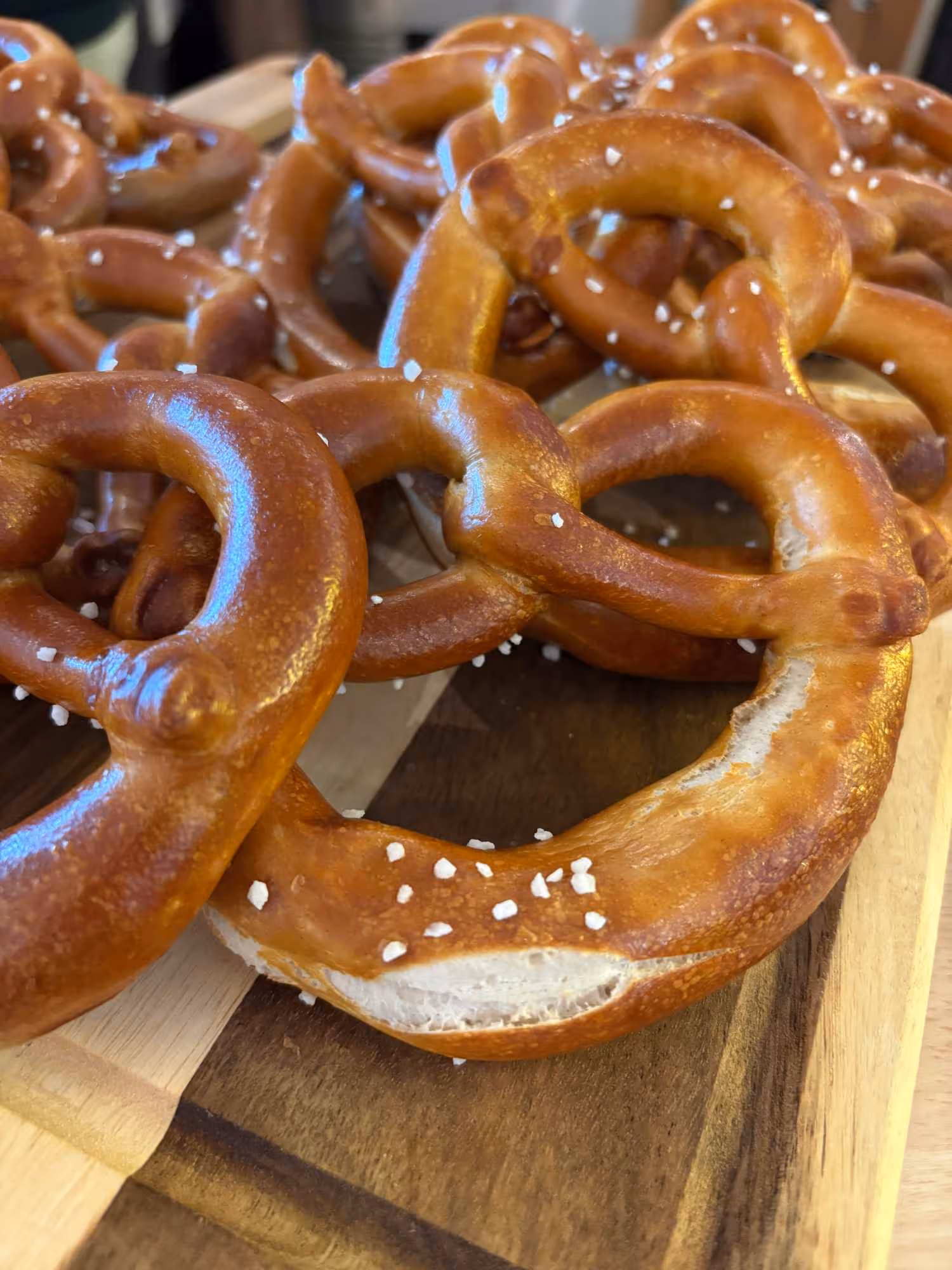 Plusieurs bretzels traditionnels dorés avec des grains de sel posés sur une planche en bois.