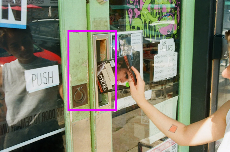 A photo of the front door with someone dropping off a movie through the door slot. There is a pink square outlining the door slot and the ring handle, which is confusing when attempting to open the door.