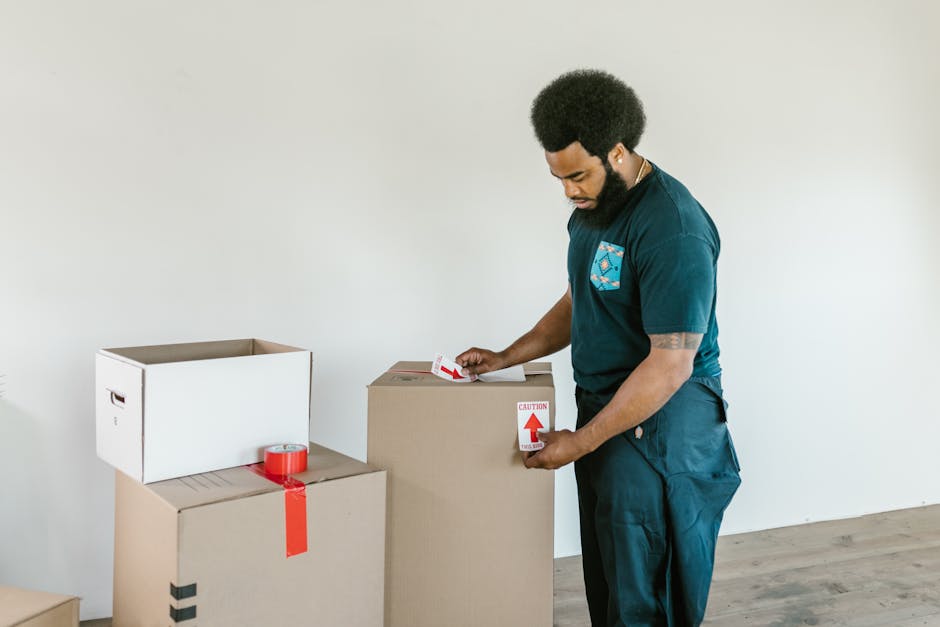 A man preparing cardboard moving boxes with caution stickers in a bright indoor setting.