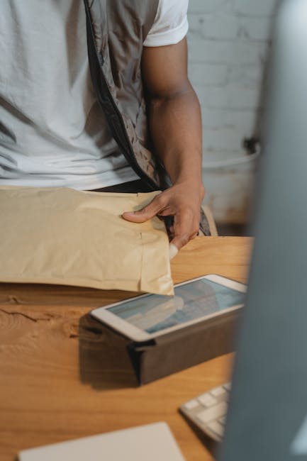 Close-up of a man holding a parcel with a tablet on a wooden desk. Indoor setting.