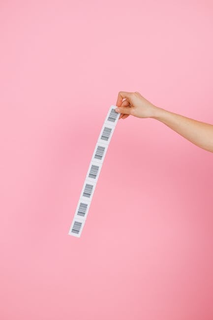 A hand holds a strip of barcodes against a pink background, creating a simple yet striking image.
