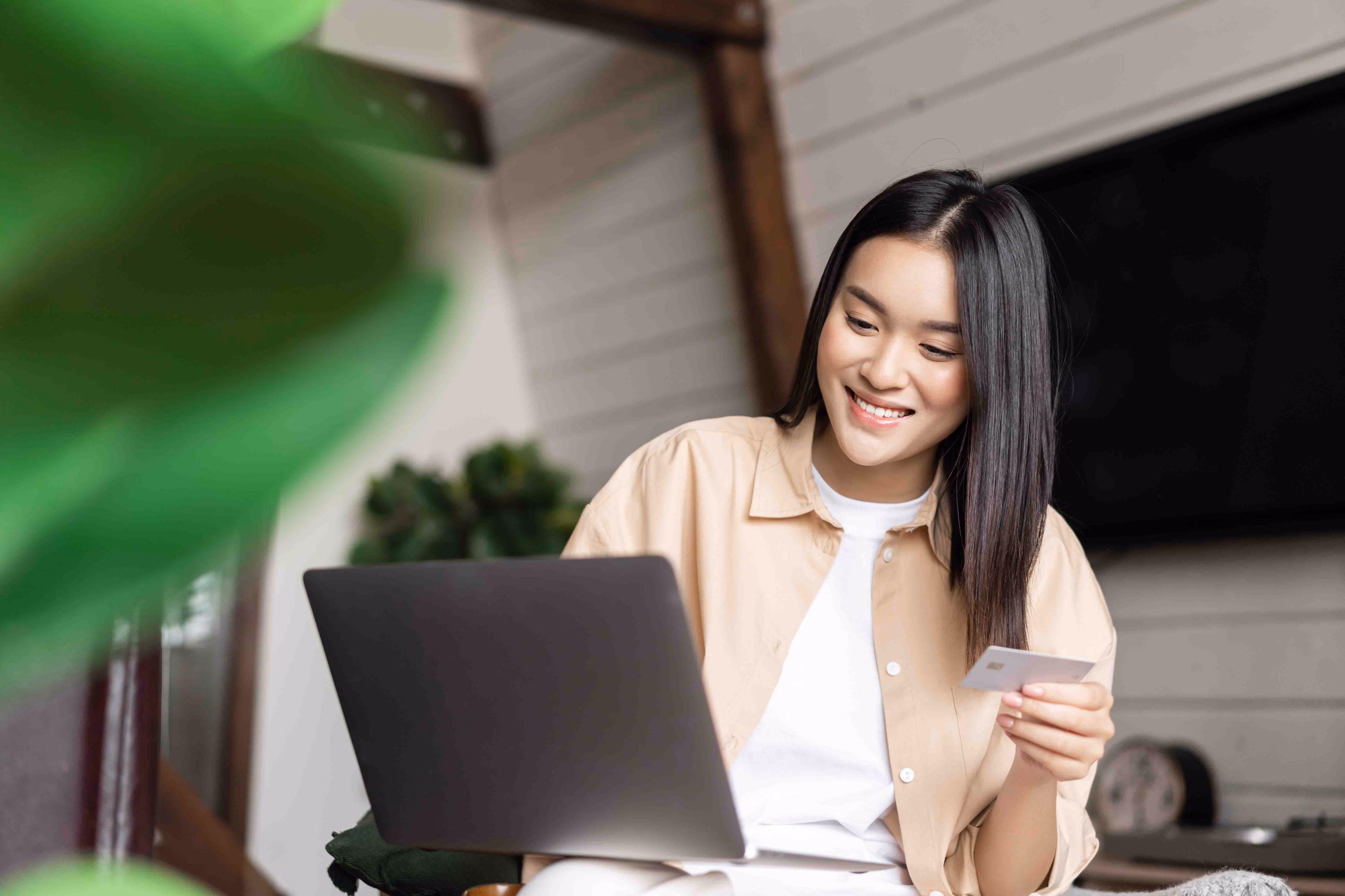 Woman using a laptop and holding a credit card, smiling while making an online payment.