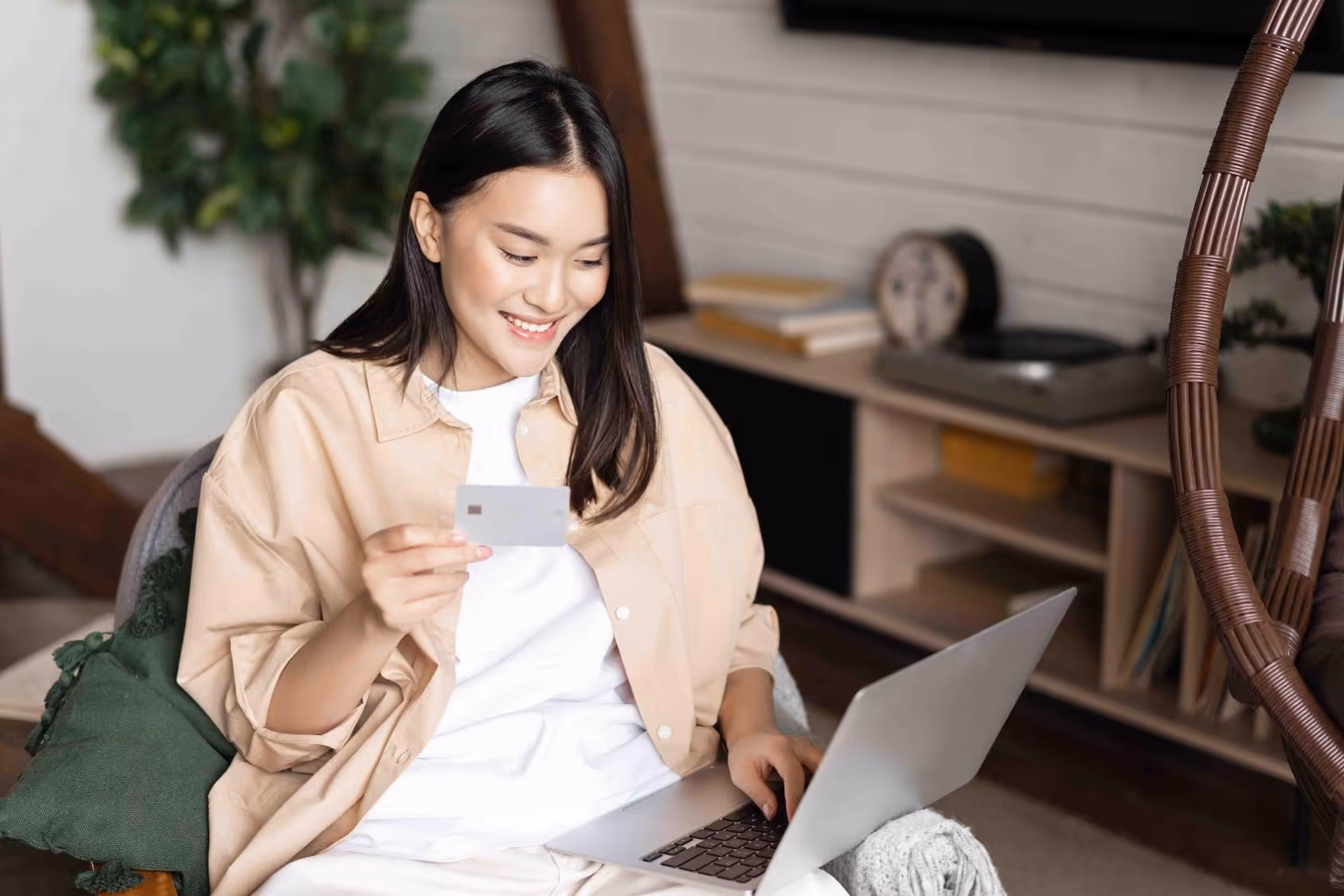 Smiling woman holding a credit card and using a laptop at home.