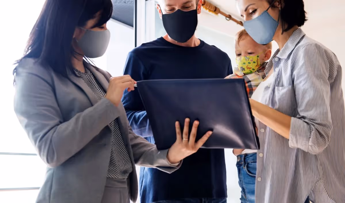 Family wearing masks reviewing documents with a real estate agent.