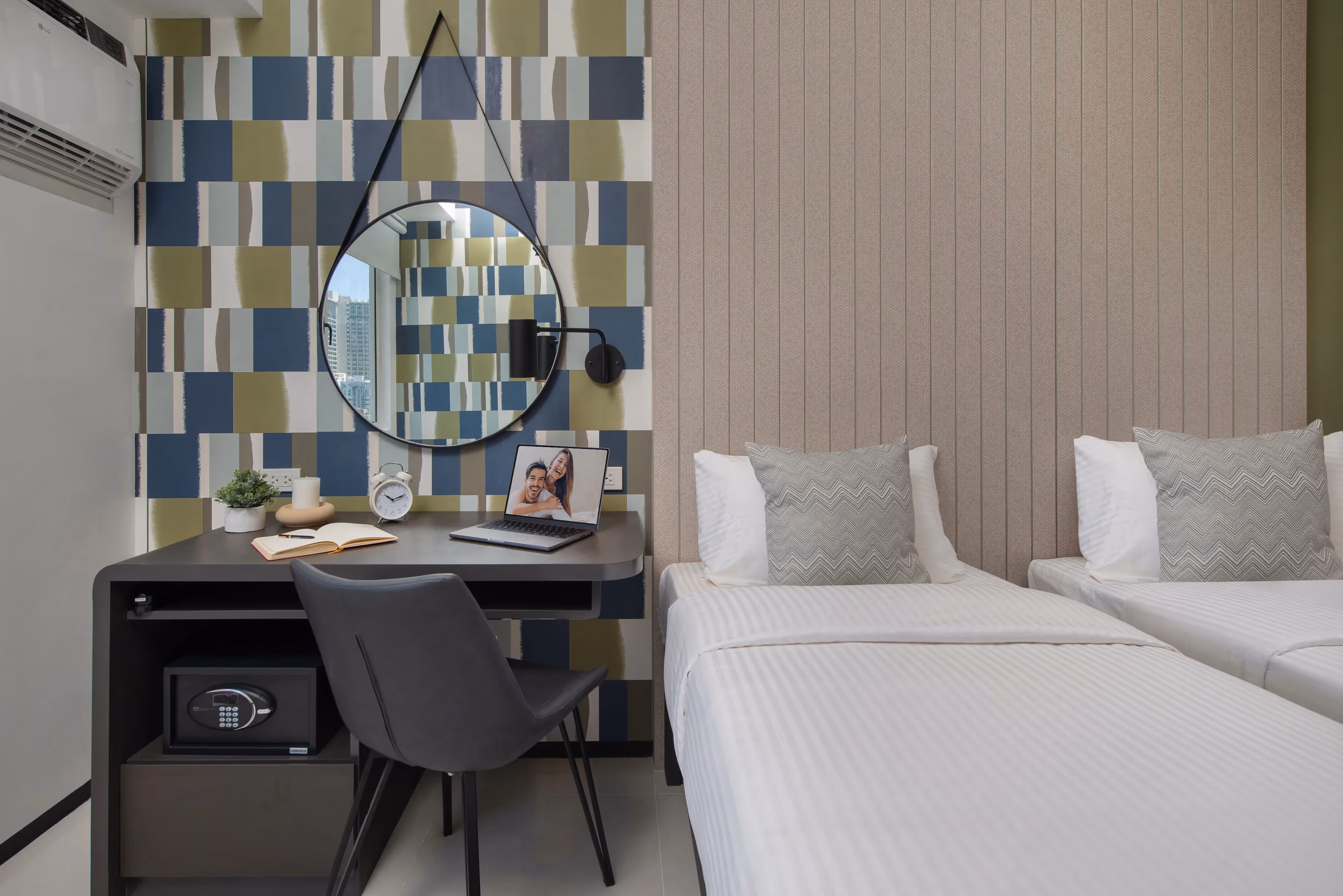 Twin beds beside a workspace with round mirror and laptop.