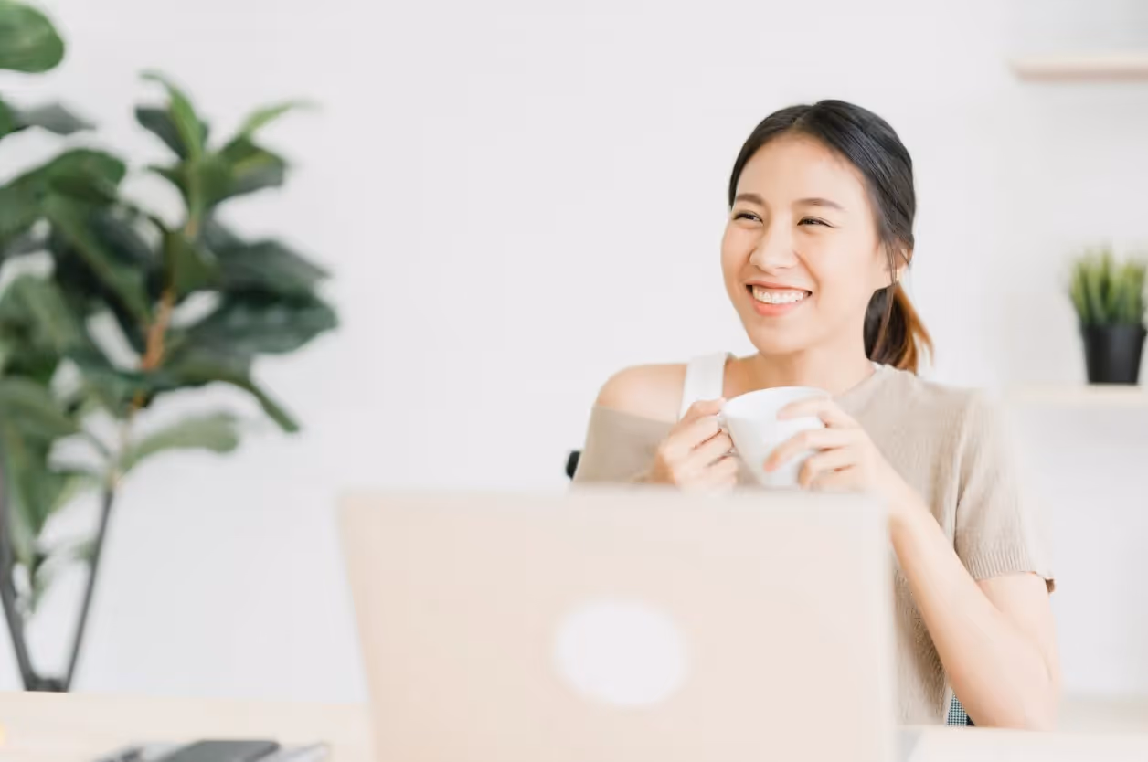 Young woman holding a mug while seated at a desk with a laptop.