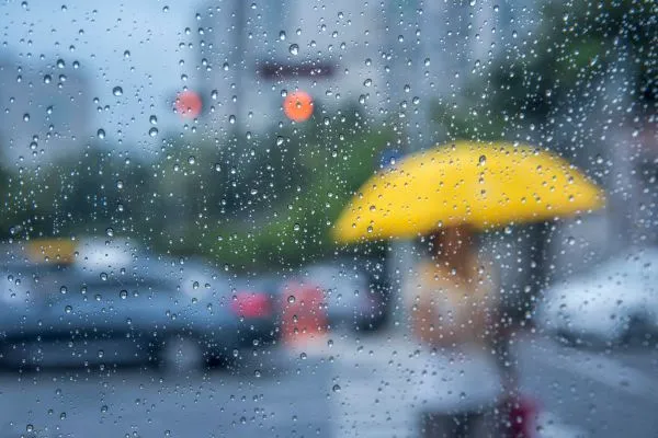 Raindrops on glass with person holding yellow umbrella outside.