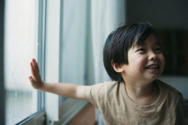 Smiling child looking out a rainy window.
