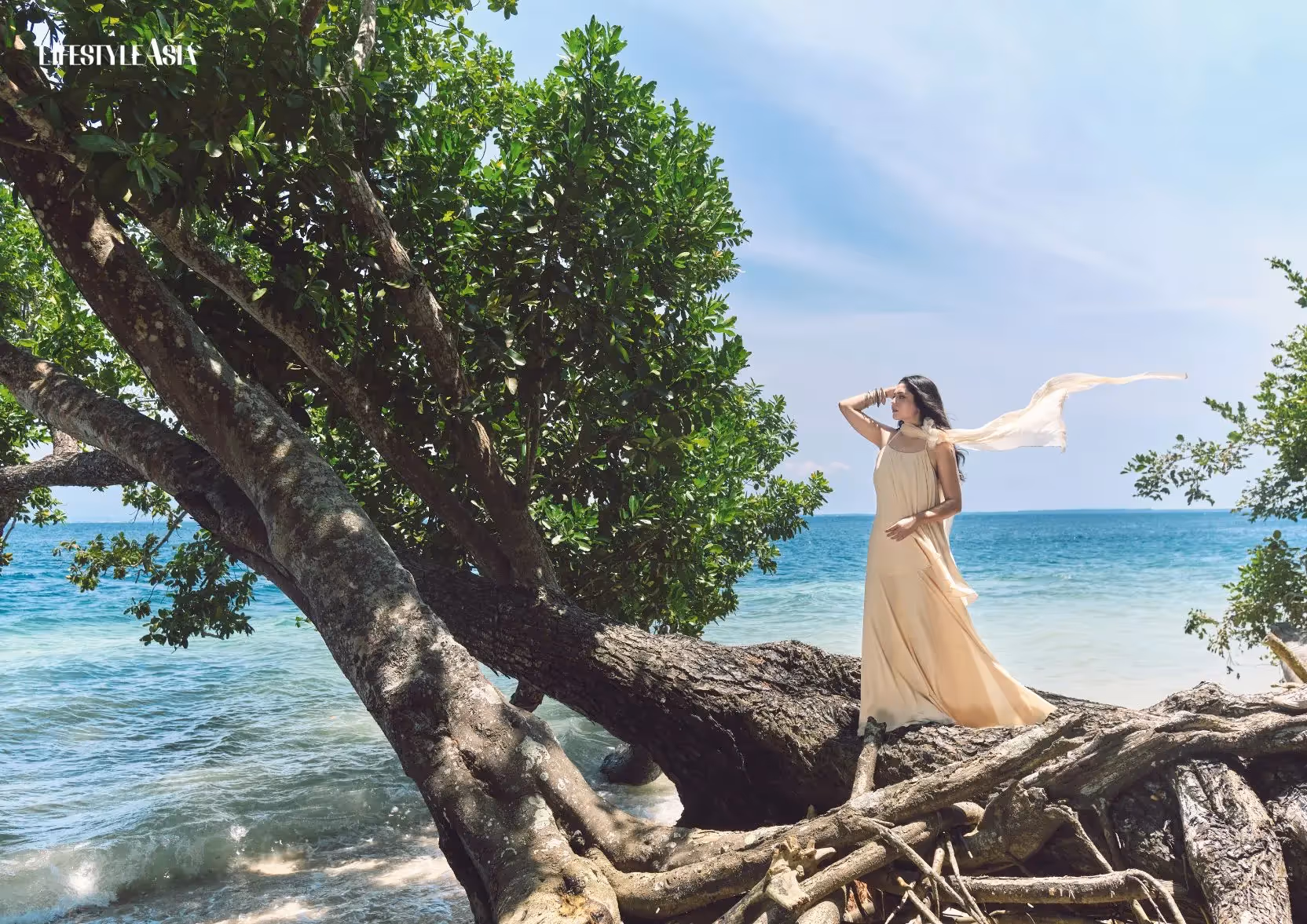 Woman in flowing dress standing on tree by the sea at tropical beach