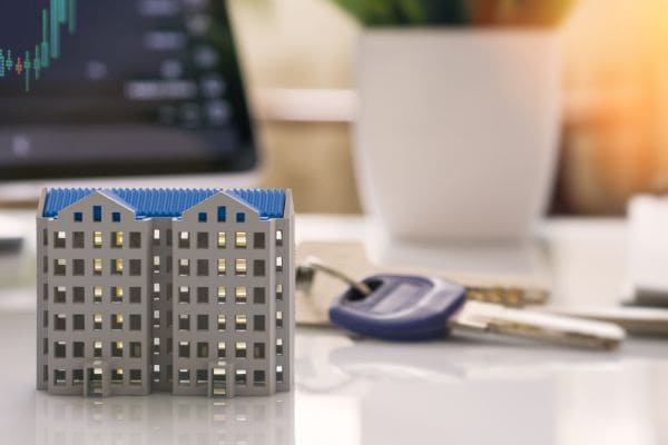 Model of apartment building beside house keys on desk