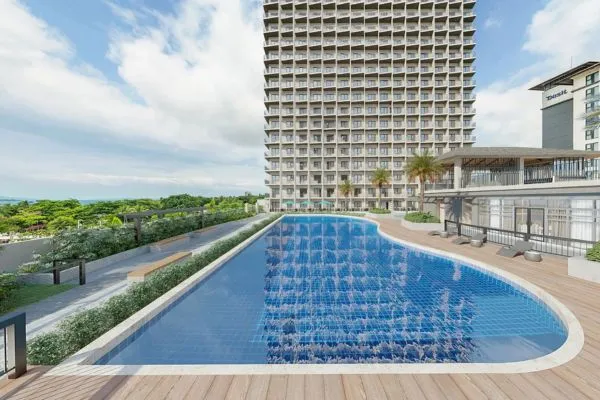 A long outdoor swimming pool next to a tall modern residential building with a wooden deck and palm trees.