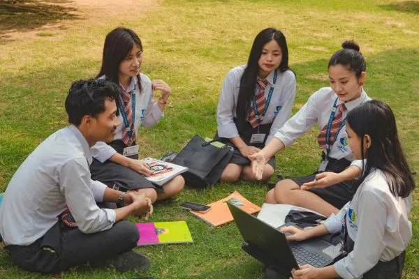 Five students in uniforms sit on grass, engaged in discussion