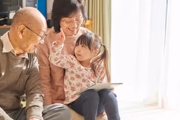 A young girl sits between an elderly couple, holding a tablet.