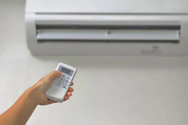 A person in a summer condo holds a remote control, adjusting the air conditioner for a comfortable indoor climate.