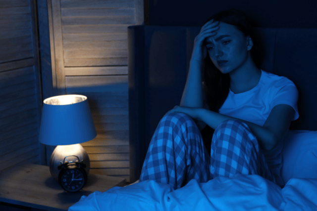 Adolescente a oscuras en su cuarto, sentada en la cama sin poder dormir