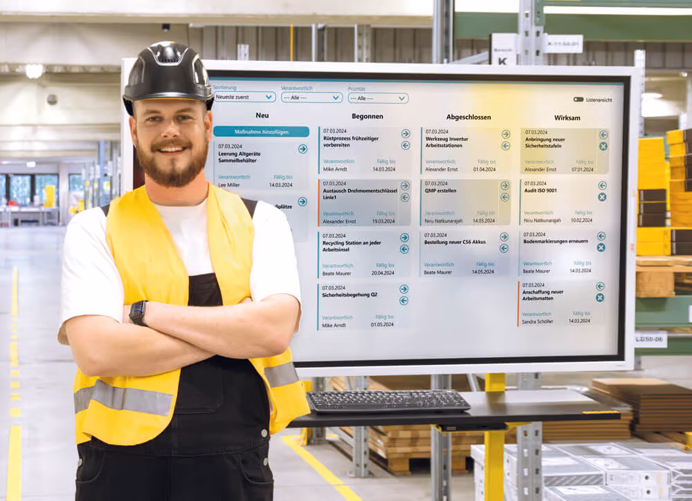 Mitarbeiter mit Sicherheitsweste und Helm vor digitalem Shopfloor-Dashboard von Peakboard in moderner Produktionsumgebung. Visualisierung von Aufgabenstatus wie 'Neu', 'Begonnen', 'Abgeschlossen' und 'Wirksam' zur effizienten Fertigungssteuerung und Prozessüberwachung.