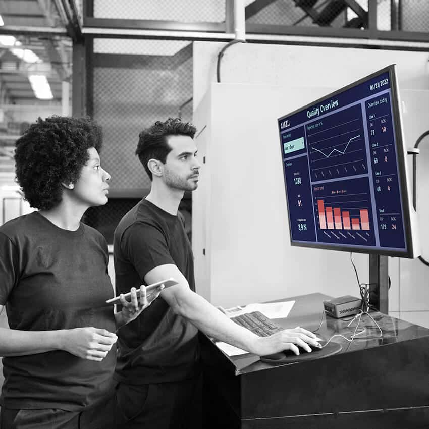 Two employees analyzing quality control data on a digital dashboard to optimize production performance.