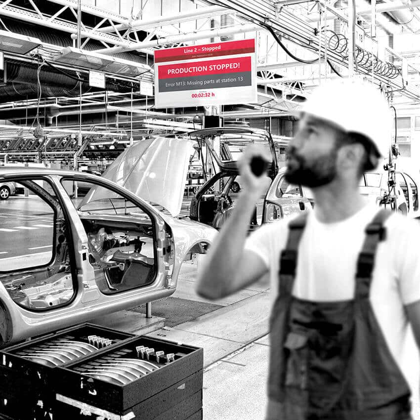 Plant employee in an automotive facility looks at a display showing a downtime warning and stop reason.
