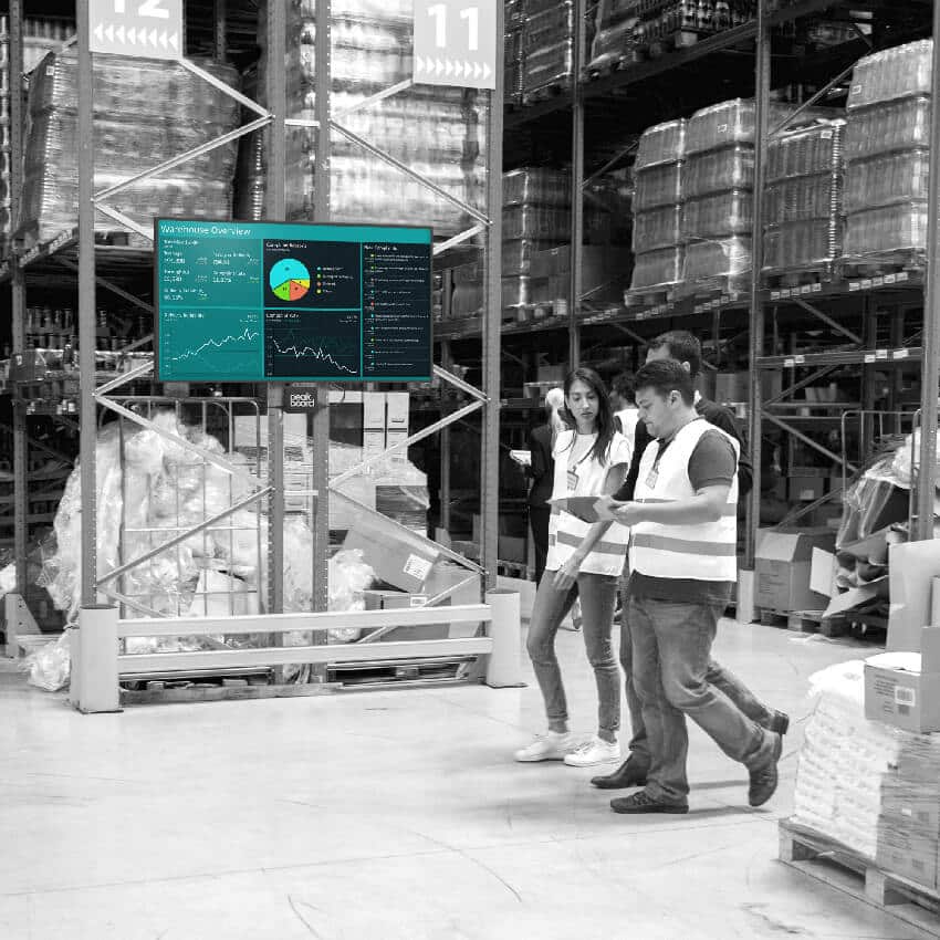 Two workers at a loading dock coordinating shipments with a real-time status board.