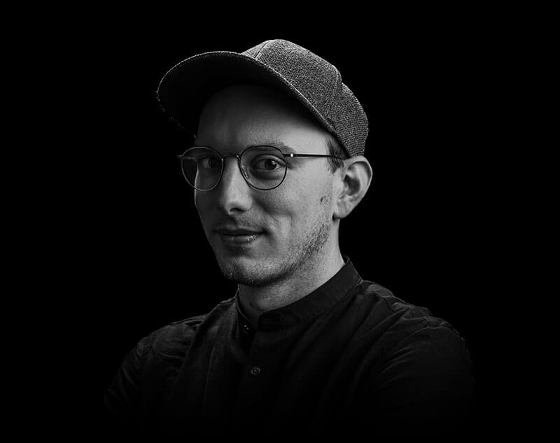 Portrait of Alex, smiling team member in the office against a dark background.
