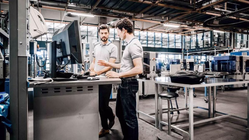 Two employees analyse production data on a computer in the manufacturing hall.