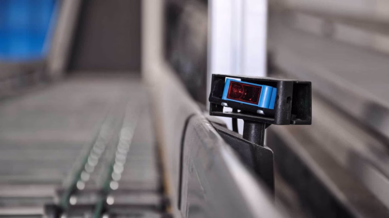 Optical sensor on a conveyor belt for automated object detection in industry.