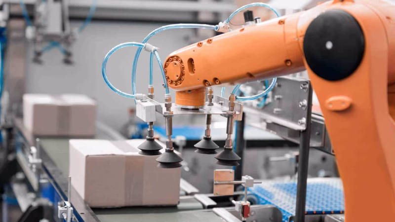 Industrieroboter mit Sauggreifer bewegt Kartons auf einem Förderband in der automatisierten Produktion.