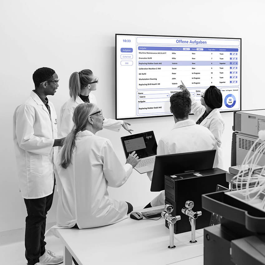 Team in Laborkleidung diskutiert Aufgaben auf einem digitalen Lean Management Board für effizientere Abläufe