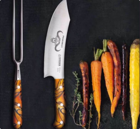 Küchenmesser und Tranchiergabel neben gegrilltem Gemüse, Beispiel für hochwertiges Kochzubehör.
