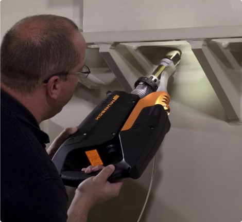 Techniker führt Materialprüfung mit mobilem Messgerät an einer industriellen Anlage durch.