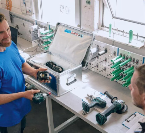Employee displays battery-powered tools and accessories at a workbench in the workshop.