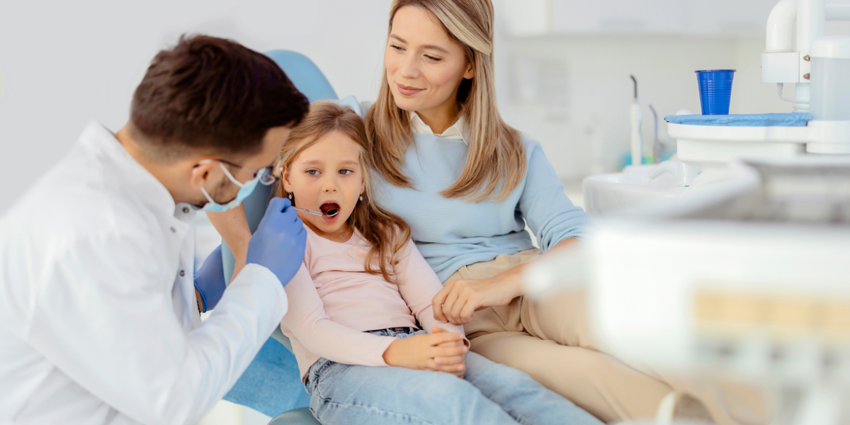 A dentist checking a young child's teeth with a supportive parent nearby in a well-lit, modern dental clinic, emphasizing comprehensive family-friendly dental care.