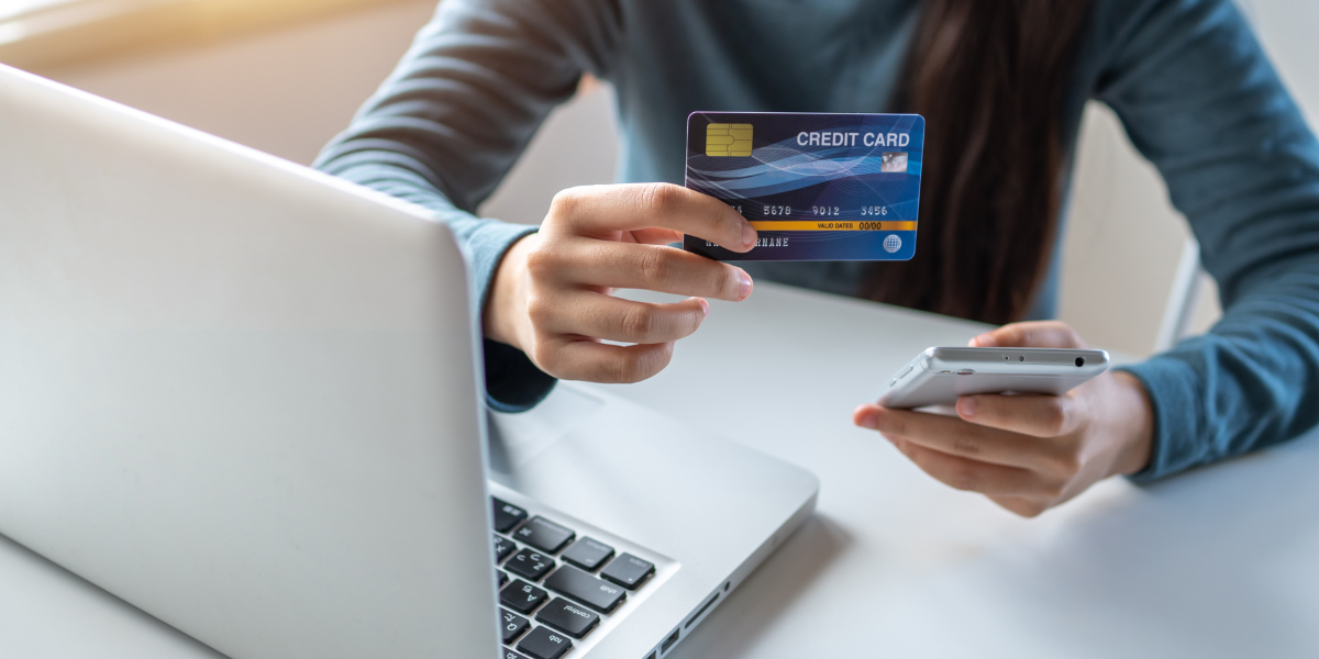 A person holding a credit card and smartphone while using a laptop, representing smart financing and payment options