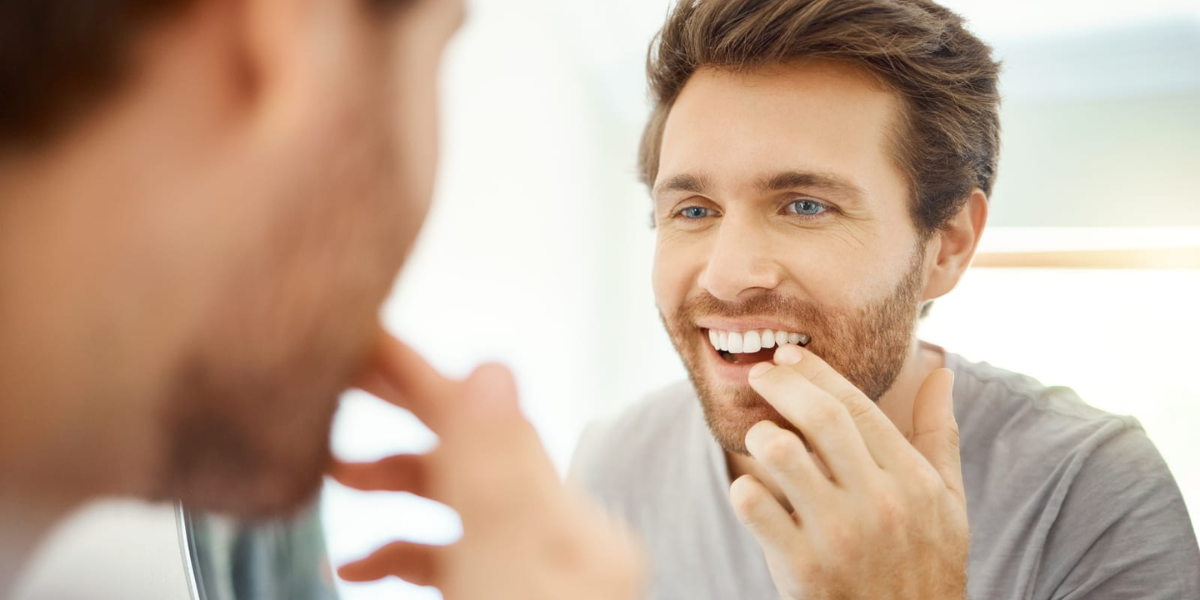A happy man looking at his reflection and smiling after improving his dental care routine, feeling more confident and at ease about oral health.