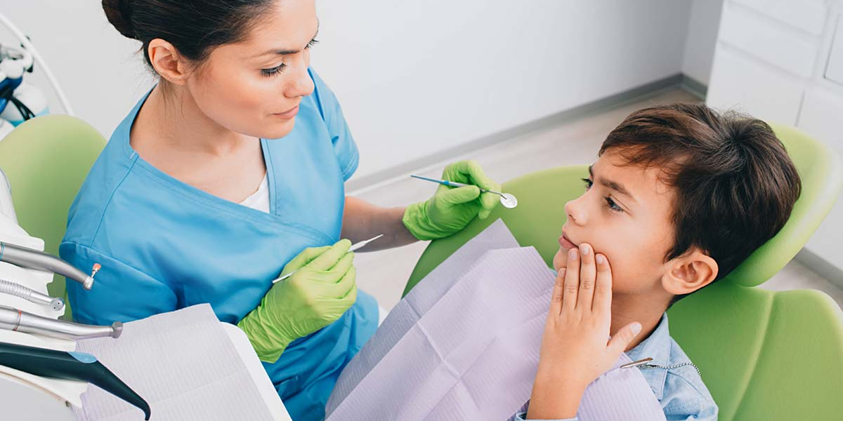 A female dentist examining a young boy with a toothache during an emergency dental visit.