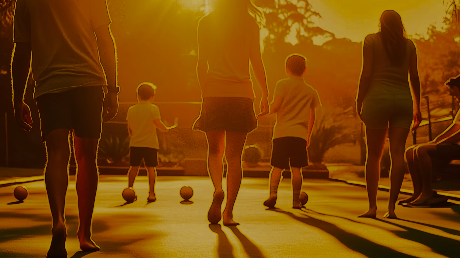 Silhouettes of adults and children playing lawn bowls outdoors at sunset.