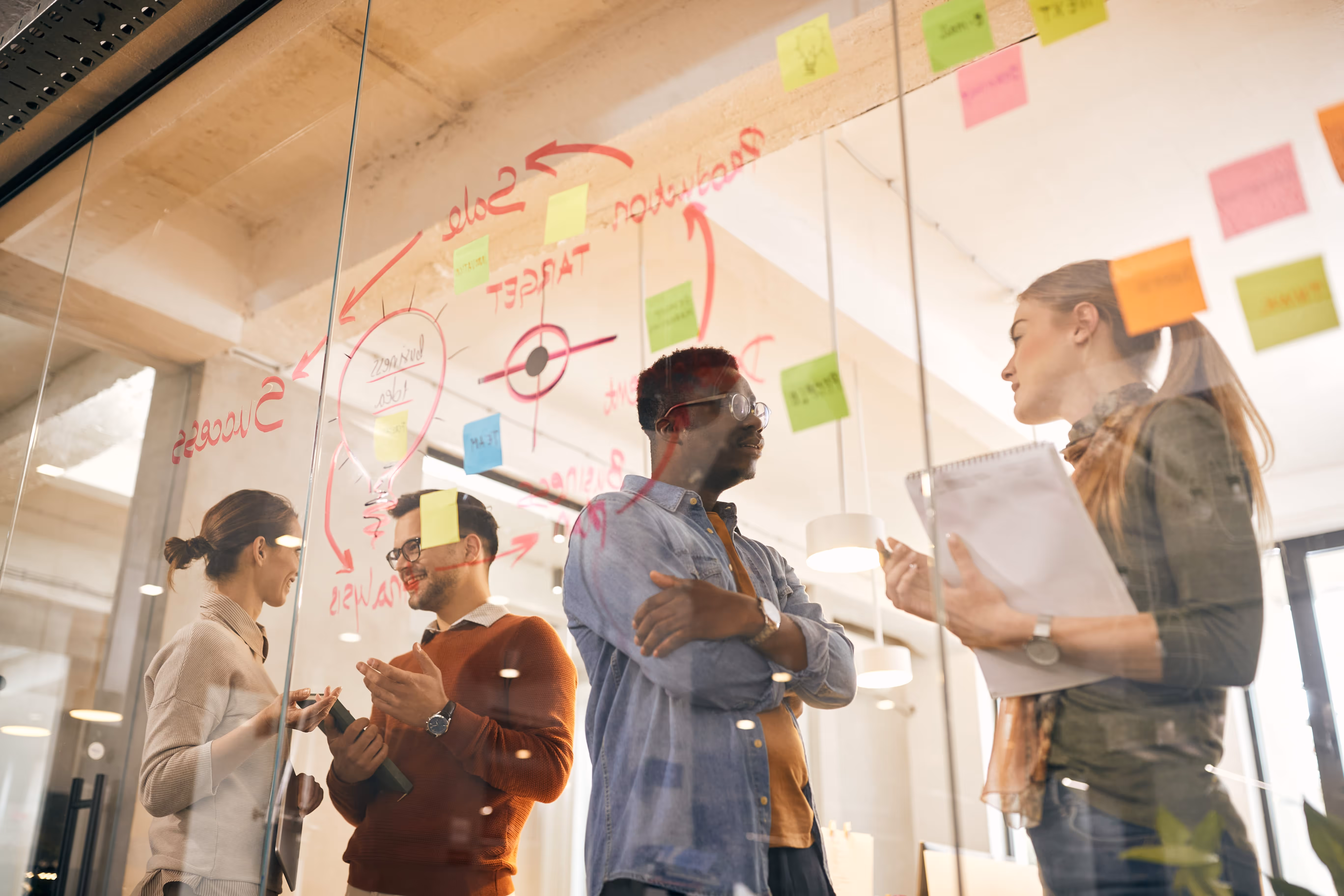 Agile Team im Gespräch vor beschriebener Glaswand während eines Lean Sherpas Workshops
