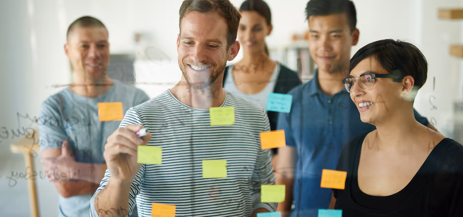 Team nach Lean Sherpas Mentoring entwickelt Ideen an Glaswand mit bunten Post-its und diskutiert agile Konzepte