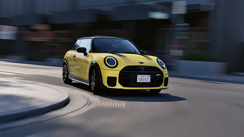 Gelber MINI Cooper C fährt dynamisch durch die Stadt – MOTORHEIMAT Wagner-Schwarz in Kirchseeon, Traunstein, Altenmarkt, Wasserburg und Oberhaching