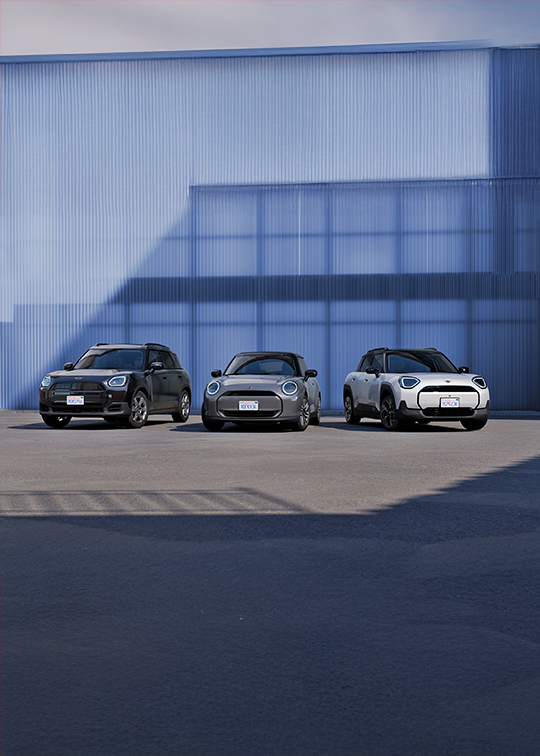 Drei MINI Modelle – MINI Countryman, MINI Cooper und MINI Aceman – nebeneinander aufgestellt vor moderner blauer Fassade bei MOTORHEIMAT Wagner-Schwarz. Präsentiert in den Standorten Altenmarkt, Traunstein, Wasserburg, Kirchseeon oder Oberhaching als Teil der neuen MINI Generation.