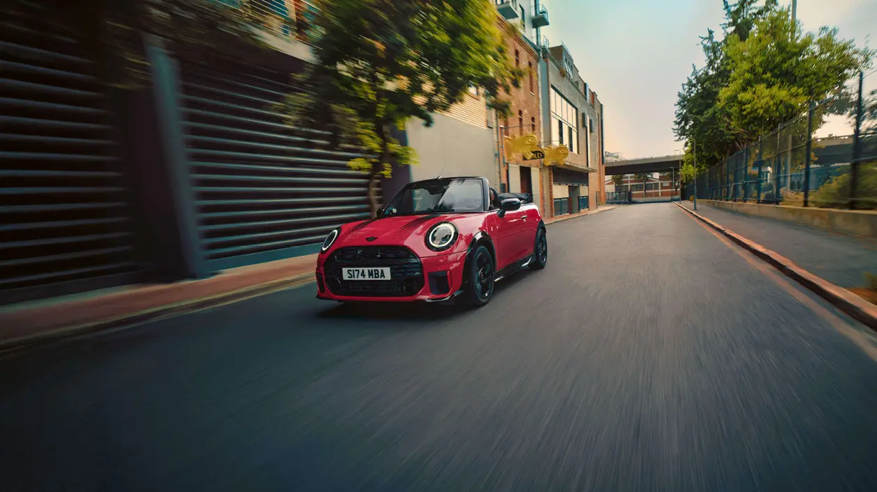 Graues MINI Cabrio mit drei Personen unterwegs auf einer sonnigen Küstenstraße – MOTORHEIMAT Wagner-Schwarz in Kirchseeon, Traunstein, Altenmarkt, Wasserburg und Oberhaching