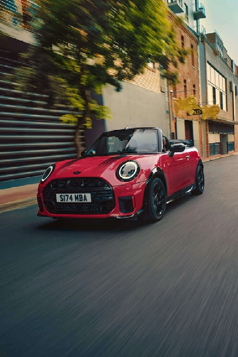 Rotes MINI Cooper C Cabrio mit schwarzen Streifen fährt durch die Stadt – MOTORHEIMAT Wagner-Schwarz in Kirchseeon, Traunstein, Altenmarkt, Wasserburg und Oberhaching