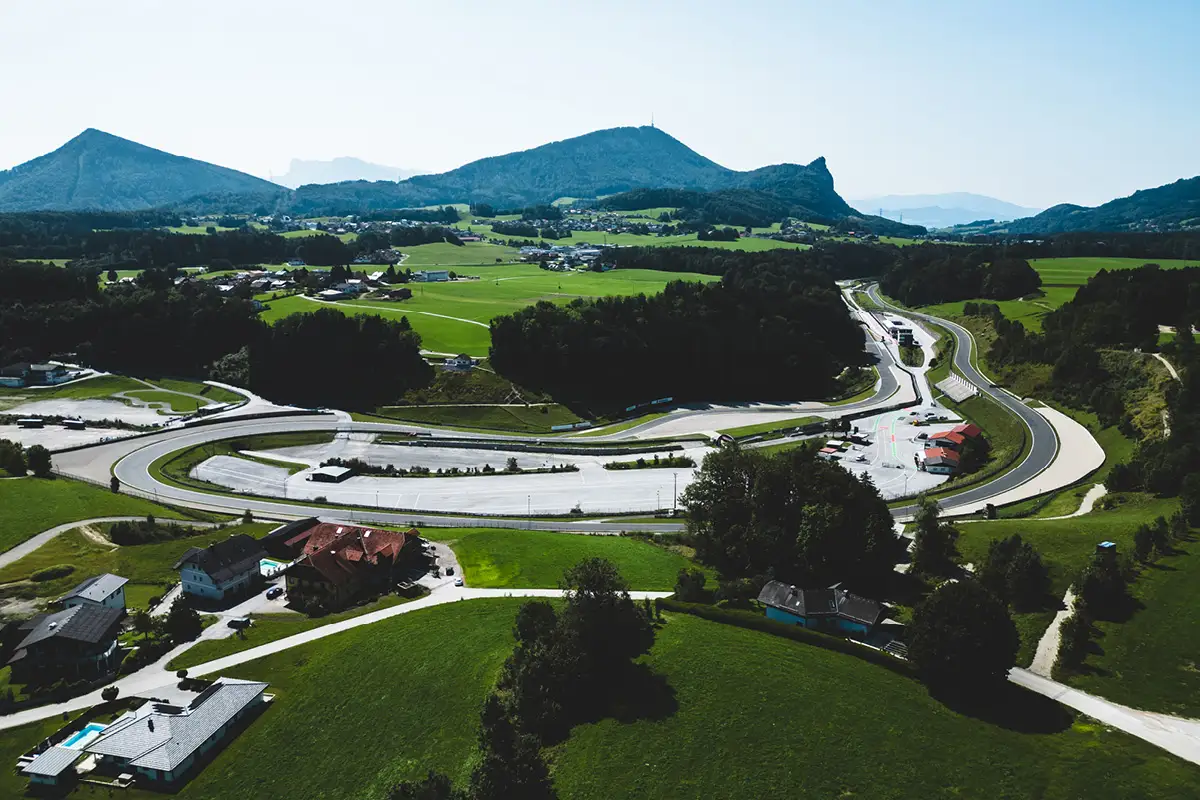 Drohnenaufnahme des Salzburgrings. Rennstrecke im Tal und Berge im Hintergrund. Wiese und Wald um die Rennstrecke herum.