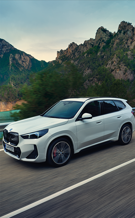 Weißer iX1 fährt bei Sonnenuntergang dynamisch auf einer Landstraße – MOTORHEIMAT Wagner-Schwarz in Kirchseeon, Traunstein, Altenmarkt, Wasserburg und Oberhaching