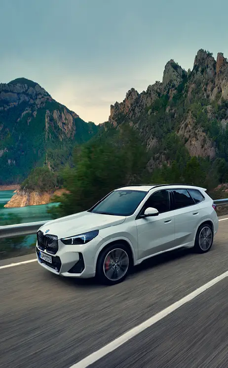 Weißer iX1 fährt bei Sonnenuntergang dynamisch auf einer Landstraße – MOTORHEIMAT Wagner-Schwarz in Kirchseeon, Traunstein, Altenmarkt, Wasserburg und Oberhaching