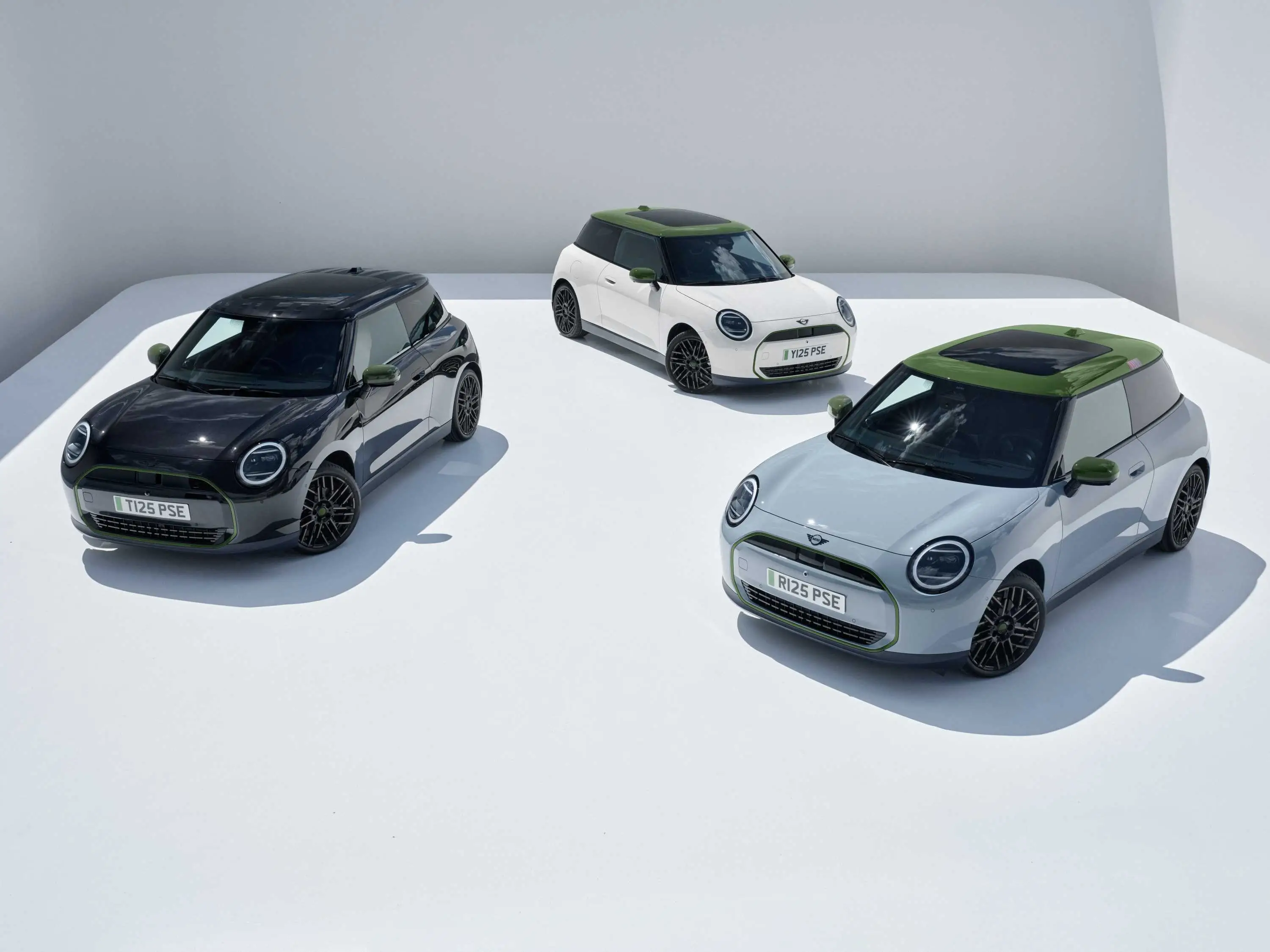Frontalansicht eines blauen vollelektrischen MINI Cooper SE mit weißem Dach in Fahrt durch eine urbane Straßenschlucht mit roter Backsteinfassade – MOTORHEIMAT Wagner-Schwarz in Kirchseeon, Traunstein, Altenmarkt, Wasserburg und Oberhaching