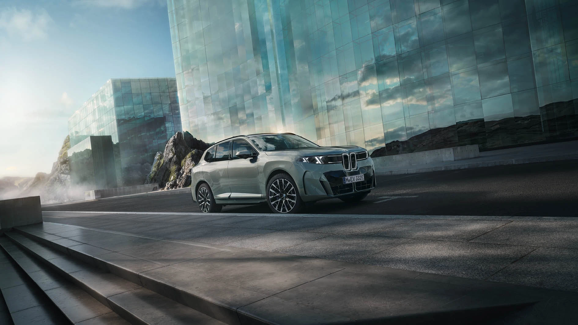 Zwei BMW X Modelle vor moderner Glasfassade, eines in Silber und eines in Petrol-Metallic an der Ladesäule – MOTORHEIMAT Wagner-Schwarz in Kirchseeon, Traunstein, Altenmarkt, Wasserburg und Oberhaching