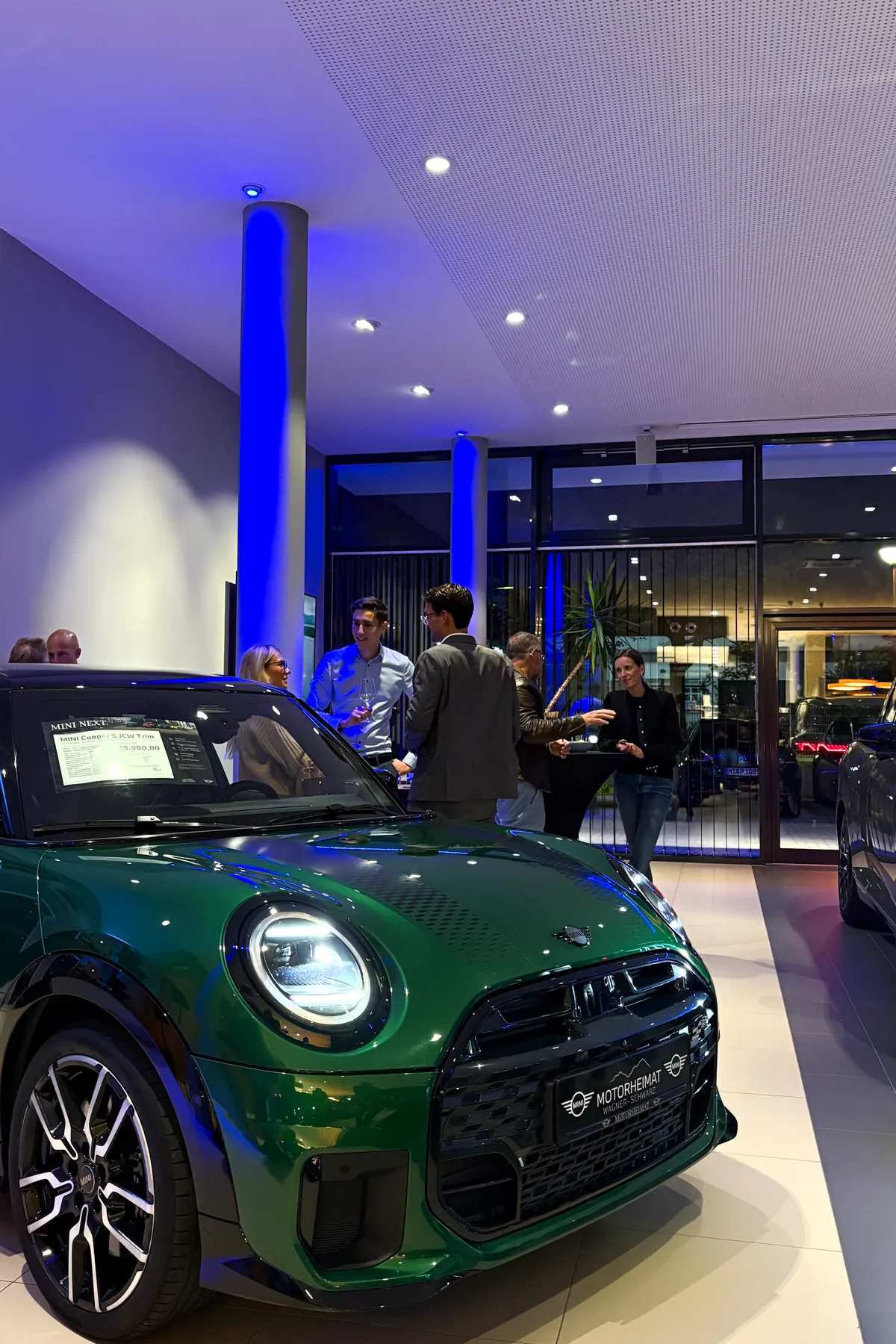 Grüner MINI Cooper S und Gäste im blau beleuchteten Showroom beim MINI Afterwork in Oberhaching